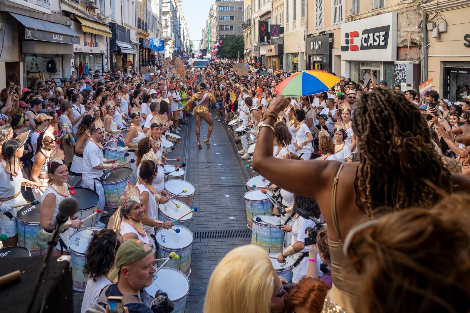 Marcos Santana in white and gold carnival kit playing snare drum in the street